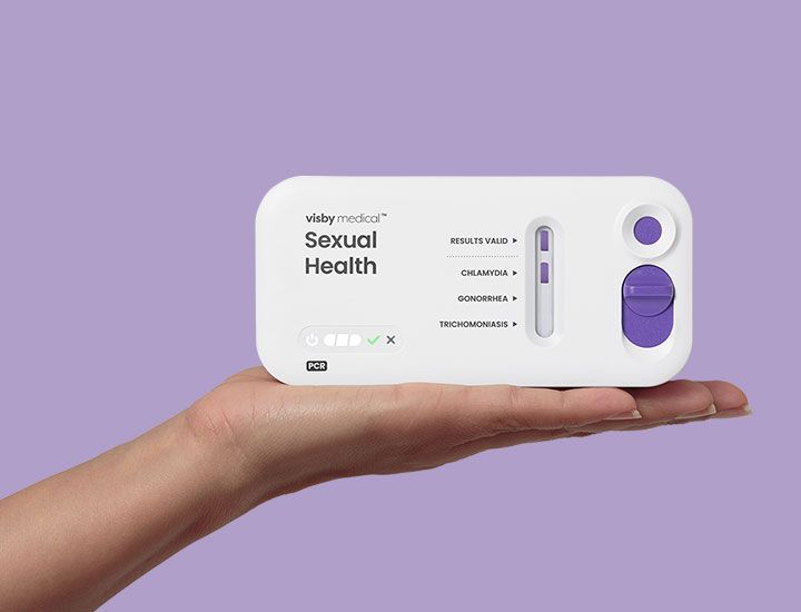 A hand holds up a Visby Medical Sexual Health Test device.