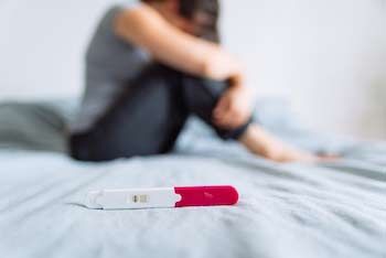 Female sitting on a bed with a pregnancy test.